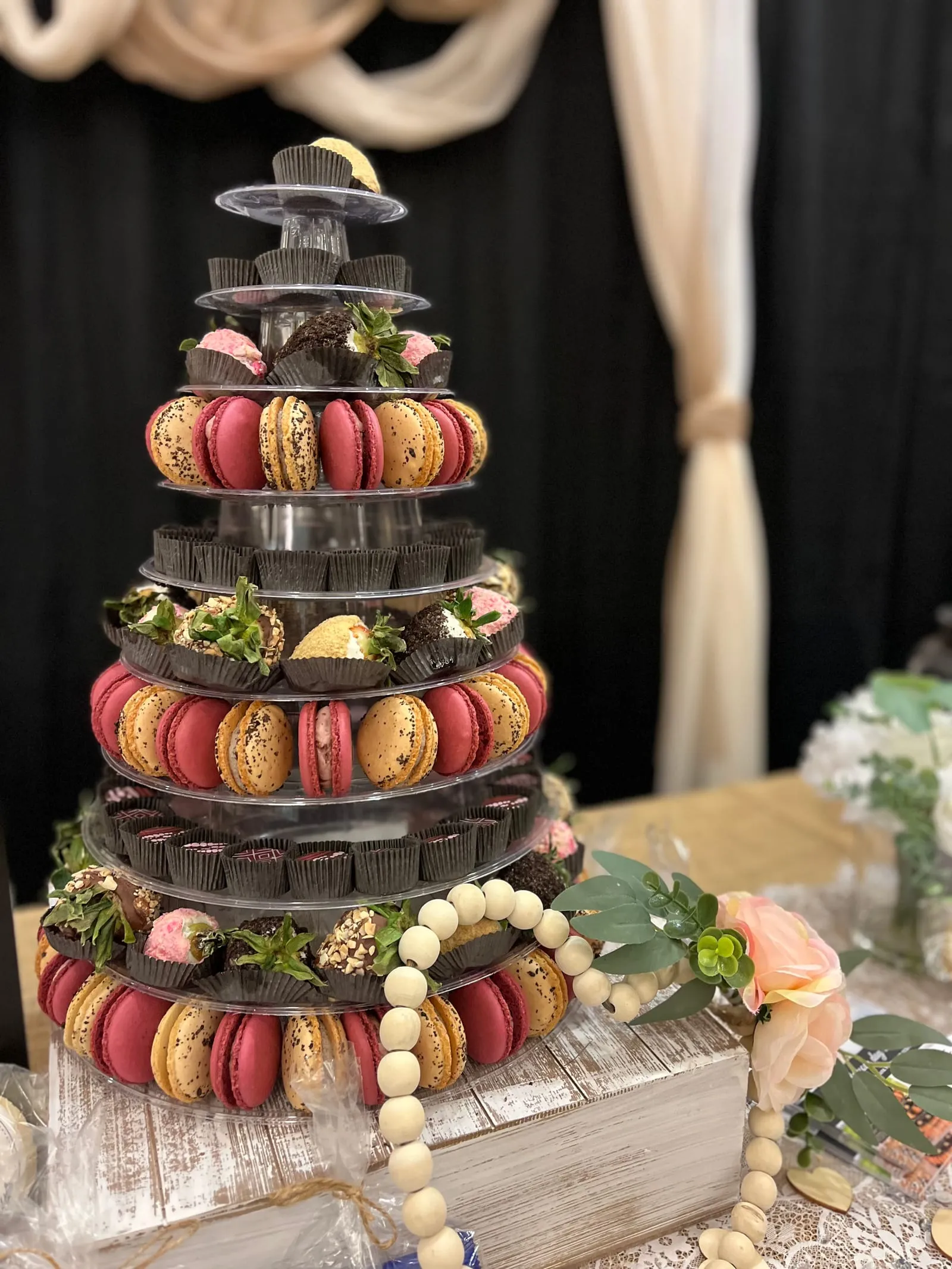 A multi-tier Event Tower of macarons, truffles, and dipped strawberries in front of draped fabric