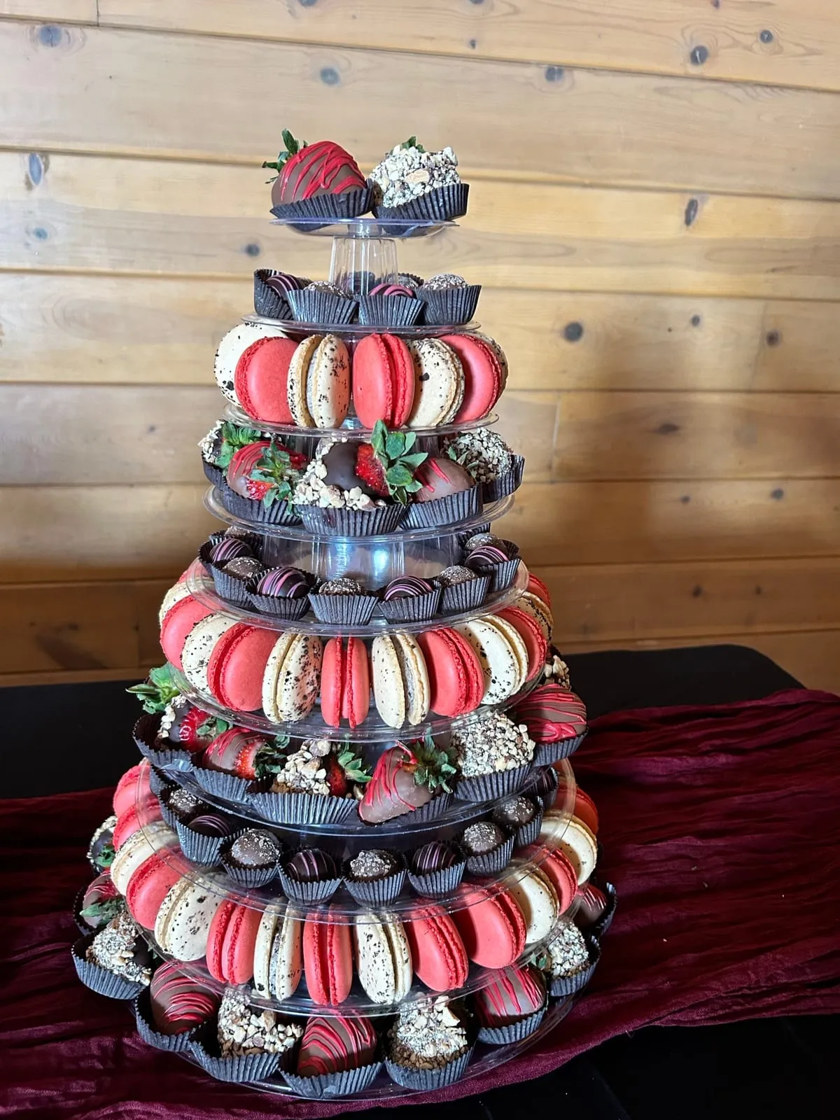 A red-and-white Event Tower of macarons and chocolate-dipped strawberries on a red velvet table