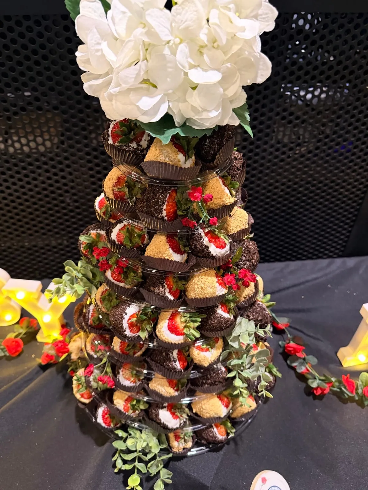 A tall artisan Event Tower of chocolate-dipped strawberries, truffles, and macarons topped with fresh white flowers