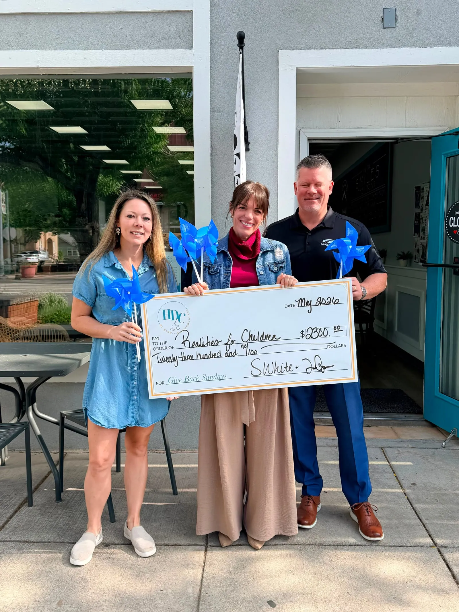 The High Desert Chocolates owners presenting a Give Back Sundays donation check to Realities for Children outside the Windsor shop
