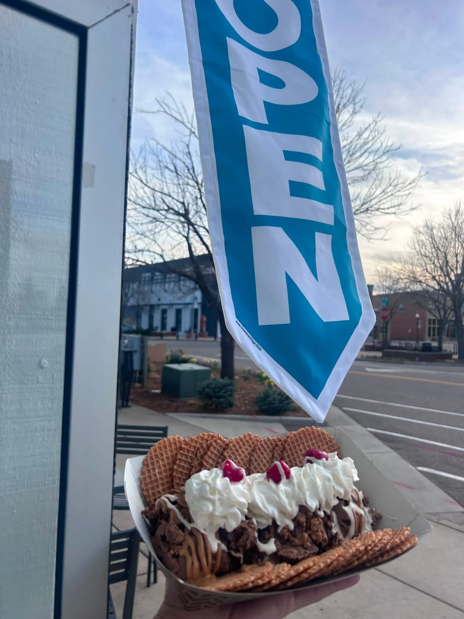 A tray of ice cream nachos held up outside High Desert Chocolates under the OPEN flag in Downtown Windsor