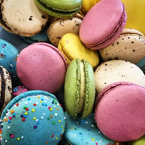 A pile of colorful macarons including blue with rainbow sprinkles