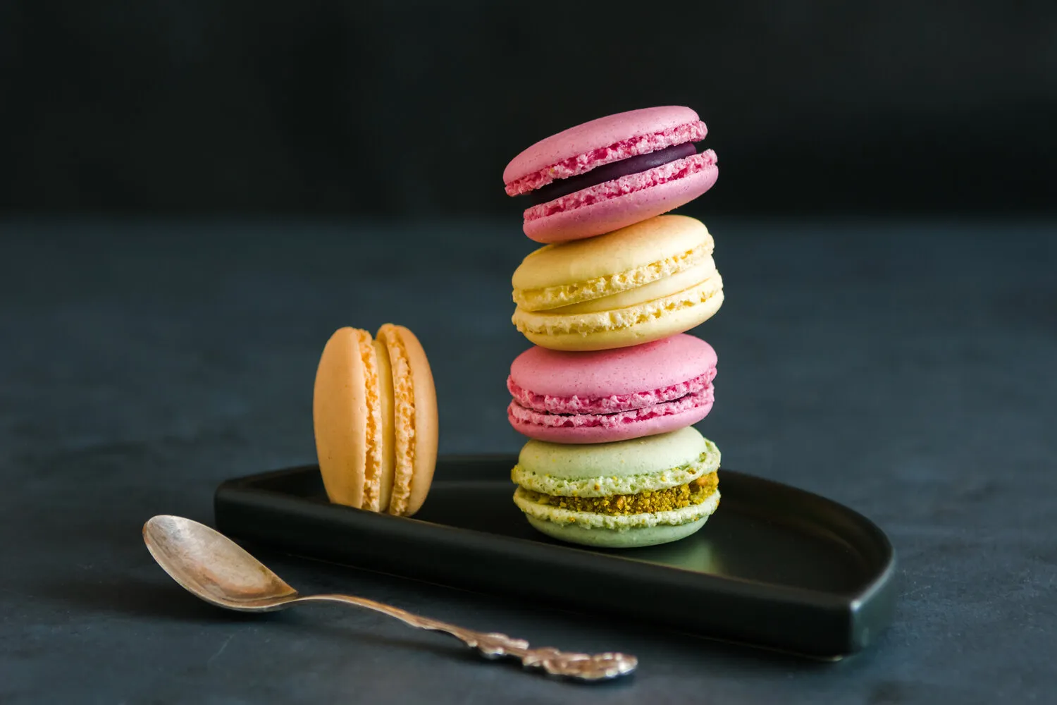 A stack of pink, yellow, and green macarons on a plate