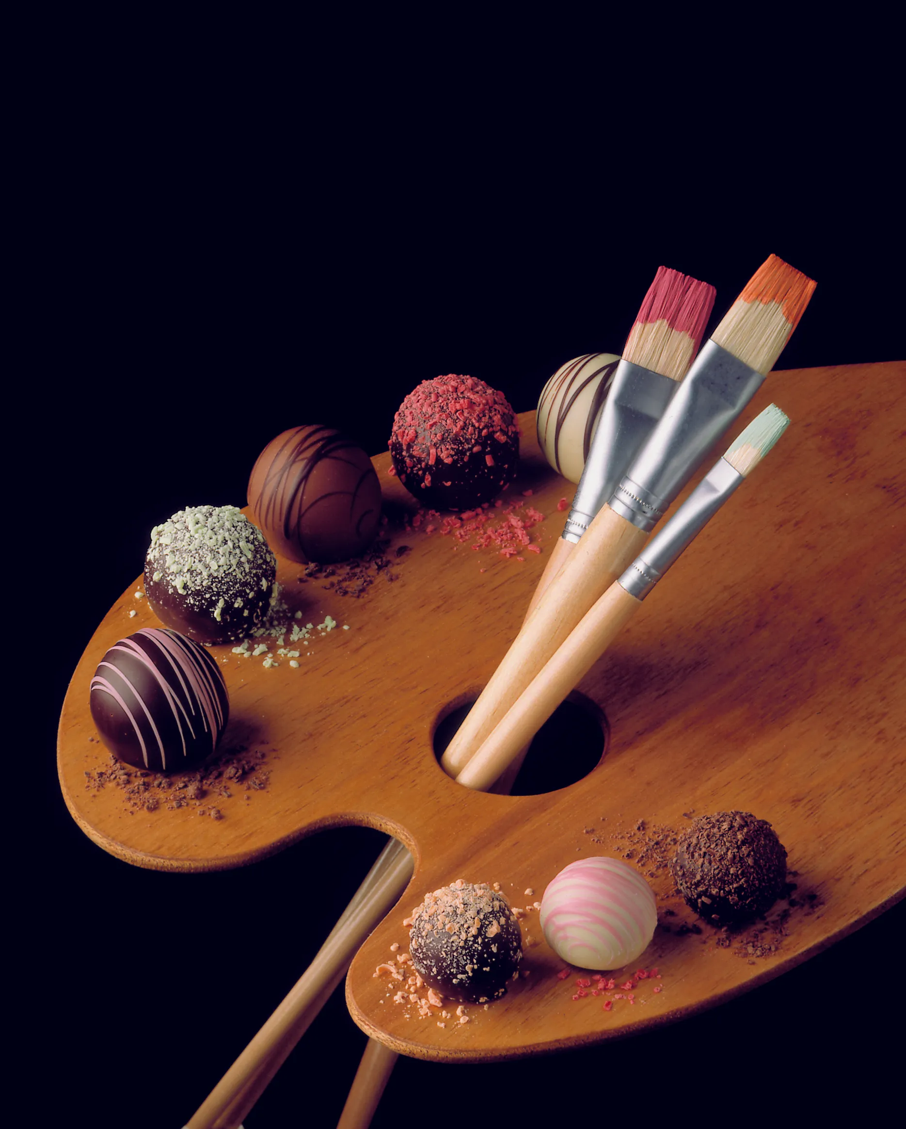 Chocolate truffles styled on a wooden artist's palette with paintbrushes