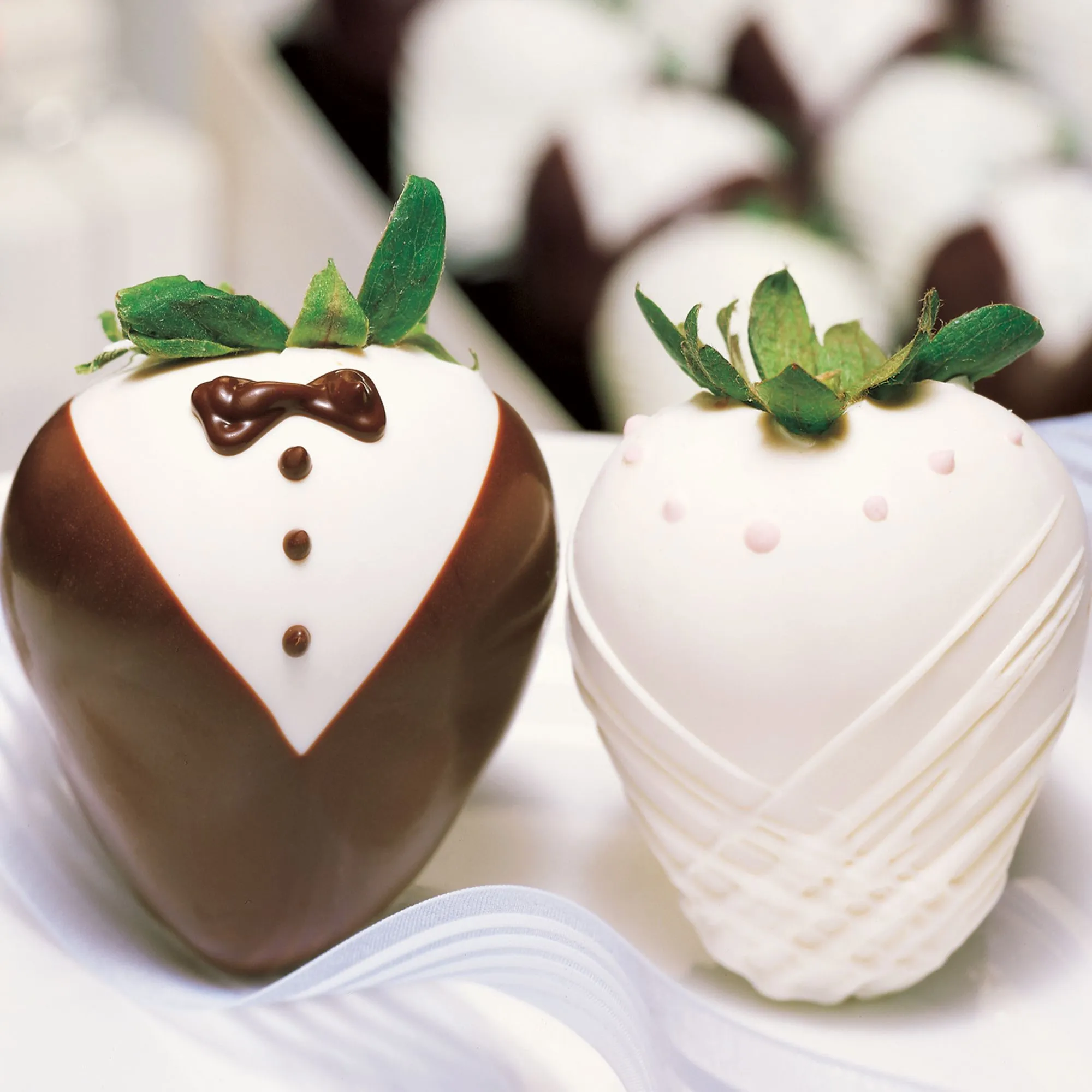 Chocolate-dipped strawberries decorated as a bride and groom on a satin-draped platter