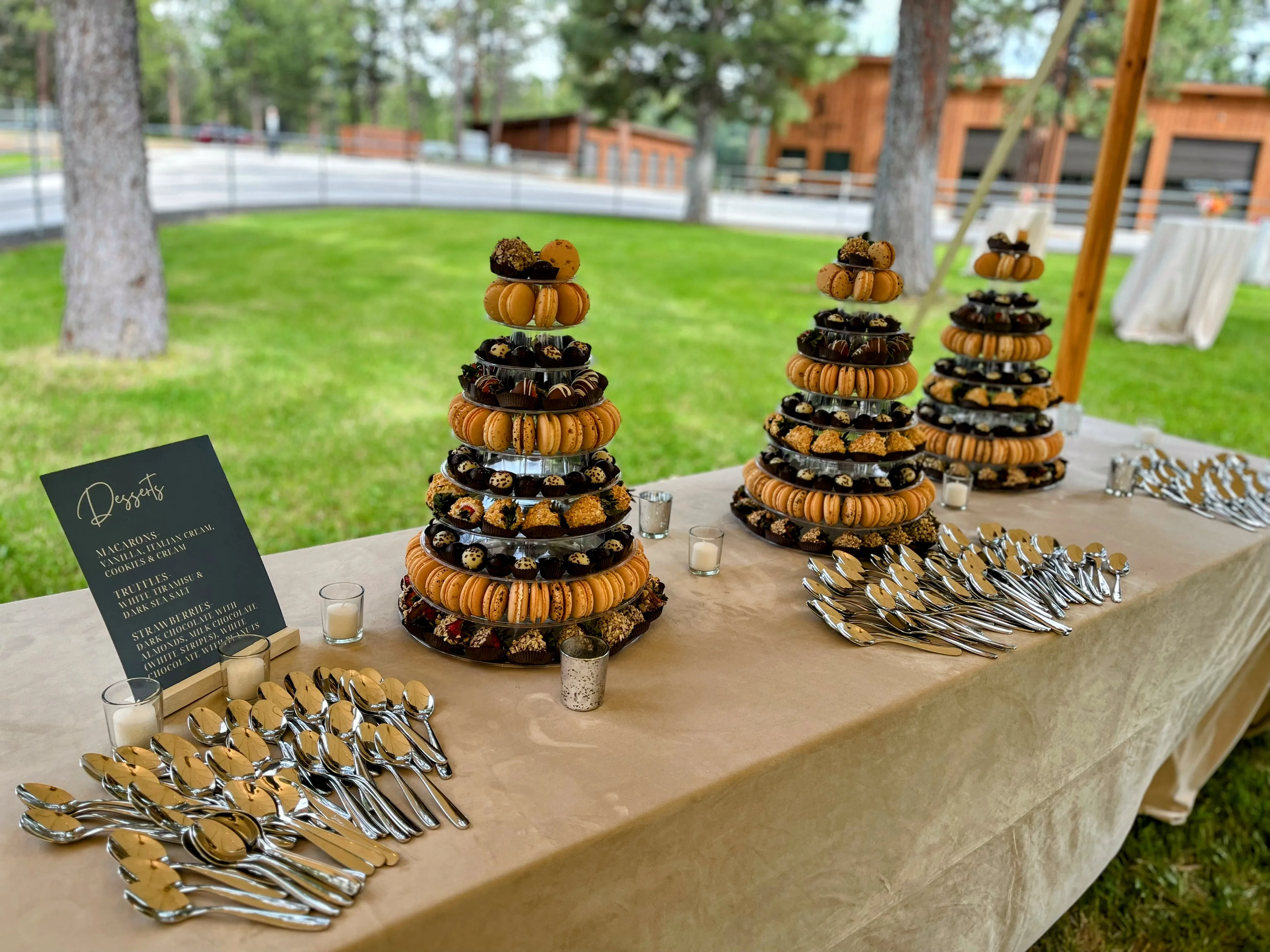 Three multi-tier dessert towers on a long outdoor catering table